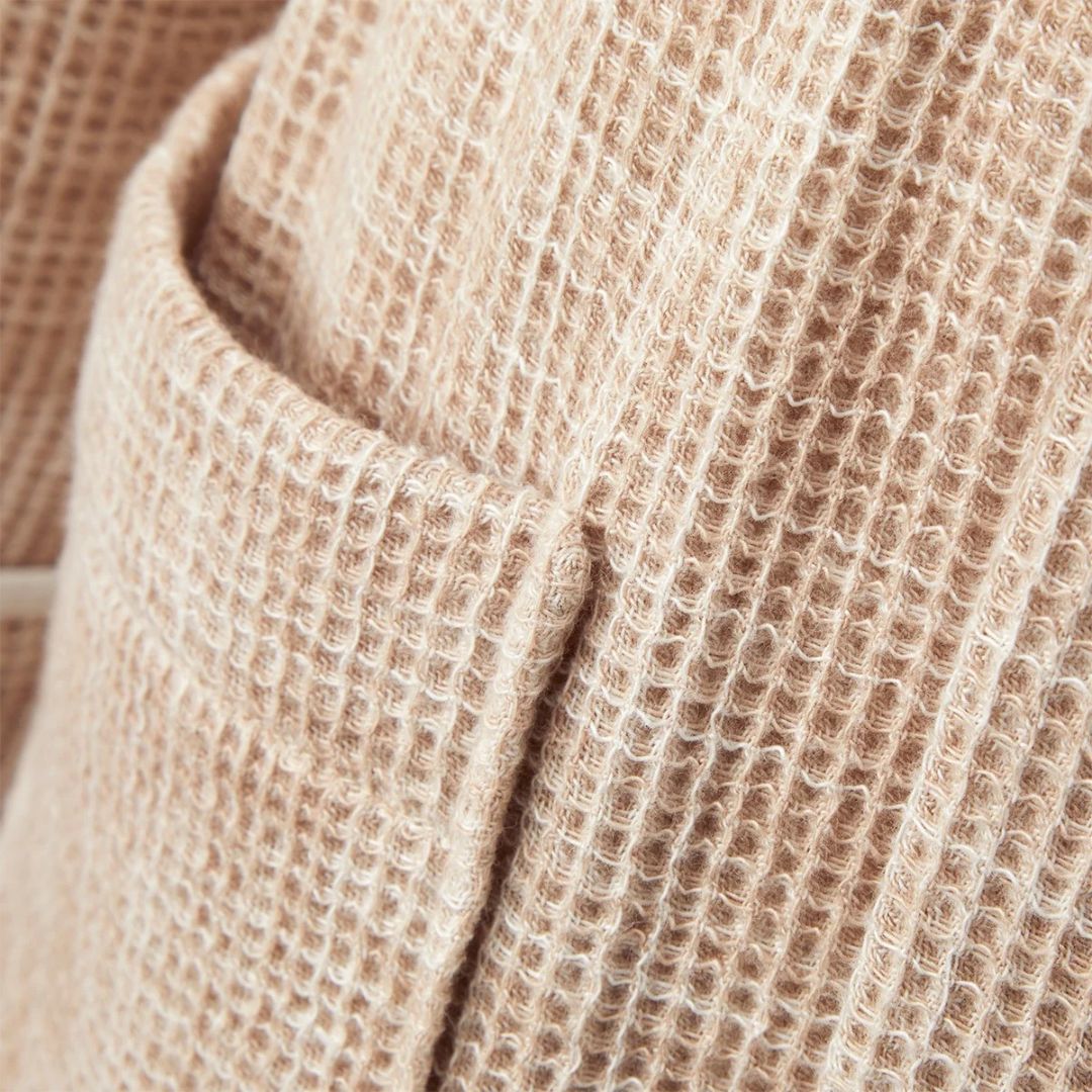 Close-up of a pocket on a beige waffle-knit Yves Delorme bathrobe.