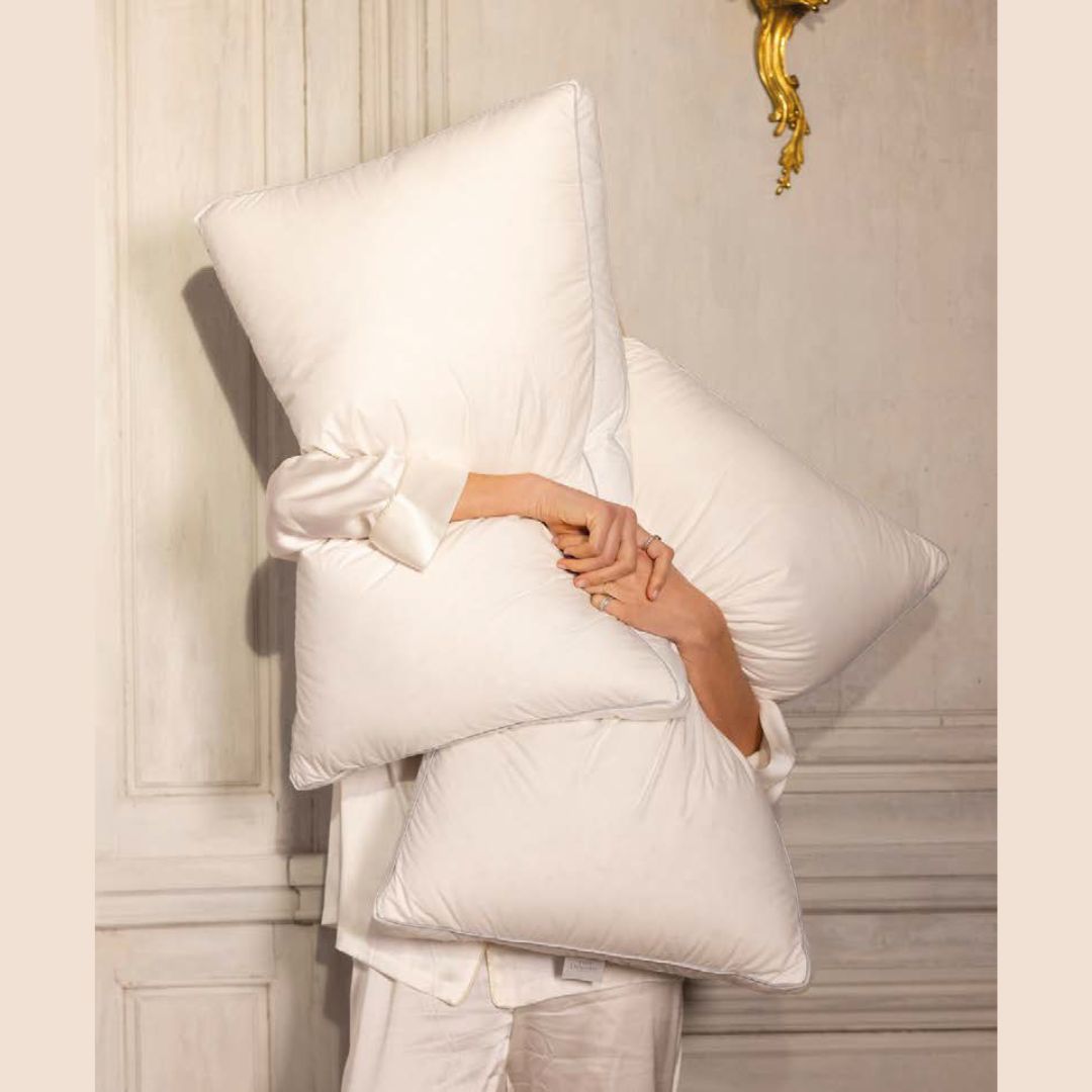 A person in white pajamas hugs luxury pillows, most of their face hidden, indoors—comfort meets cozy elegance.