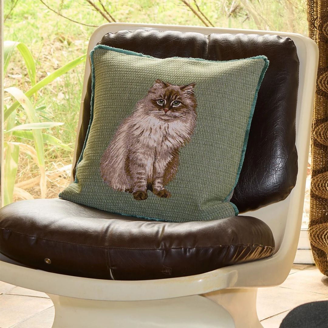 Green Yves Delorme decorative pillow featuring a feline design on a dark leather chair.