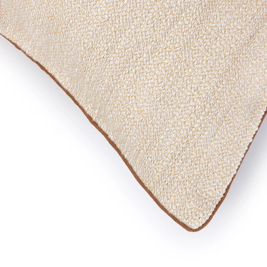 A corner of a textured, cream-colored Yves Delorme cotton jacquard tapestry pillow with brown piping.