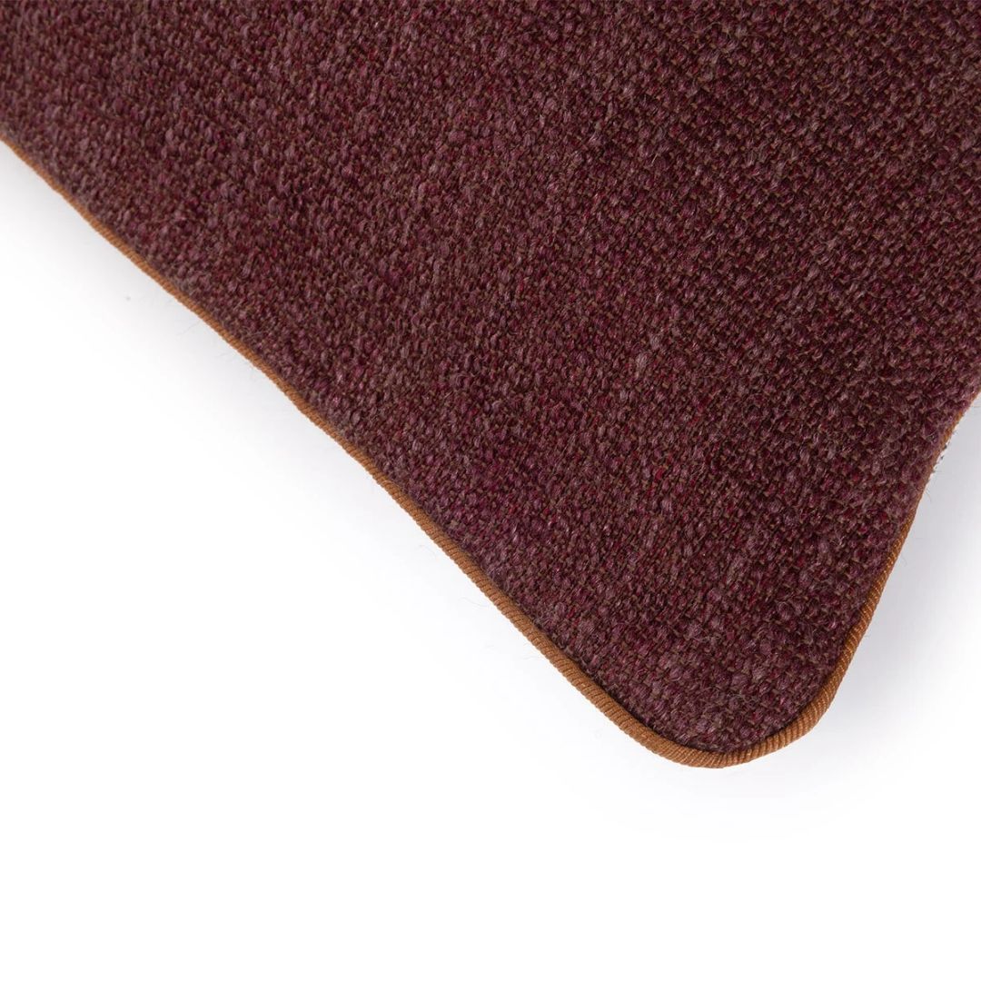 A corner of a deep burgundy Yves Delorme Charlies decorative pillow with brown piping.