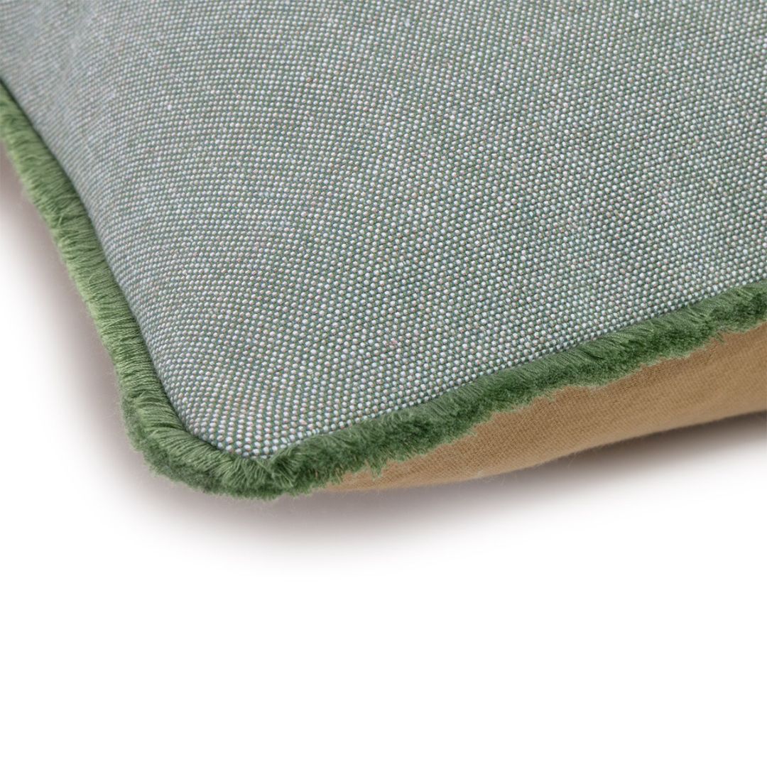 A corner of a two-toned Yves Delorme decorative pillow with a green fringe border.