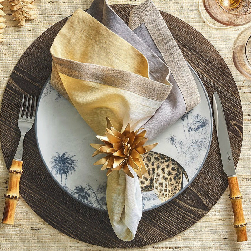 Place setting with animal-print plate, Kim Seybert bamboo-handled cutlery, and a gold napkin ring on a round placemat.