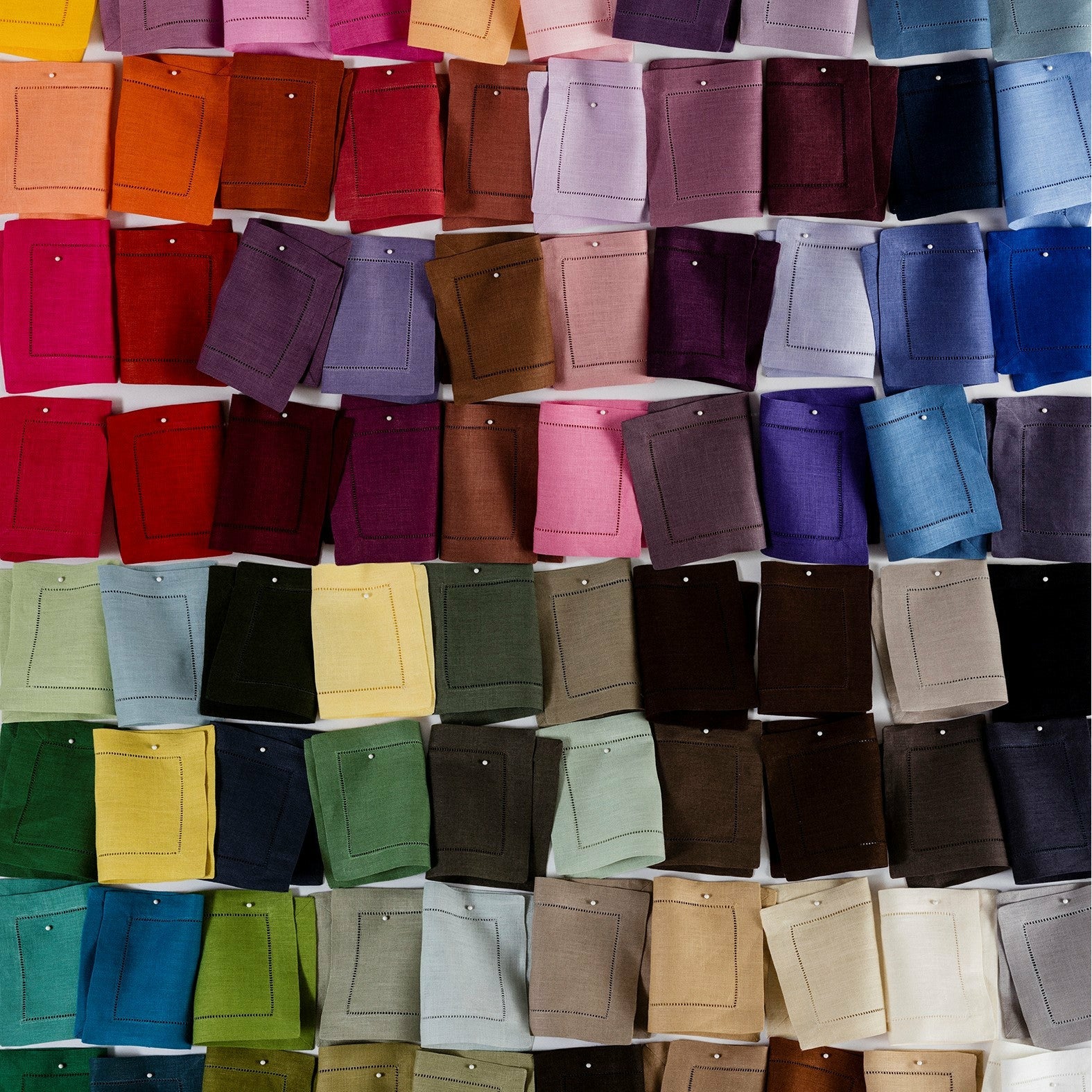 A collection of Sferra Festival table linen swatch samples displayed in a color spectrum, including a variety of solid colored napkins and placemats.
